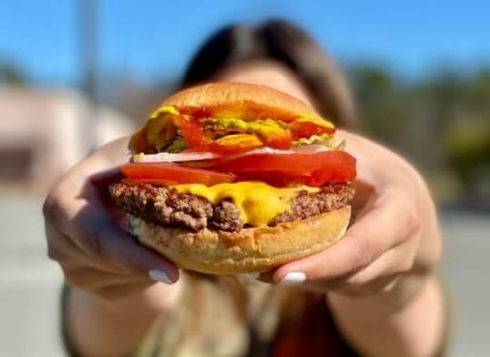 A woman hold a big juicy cheeseburger.