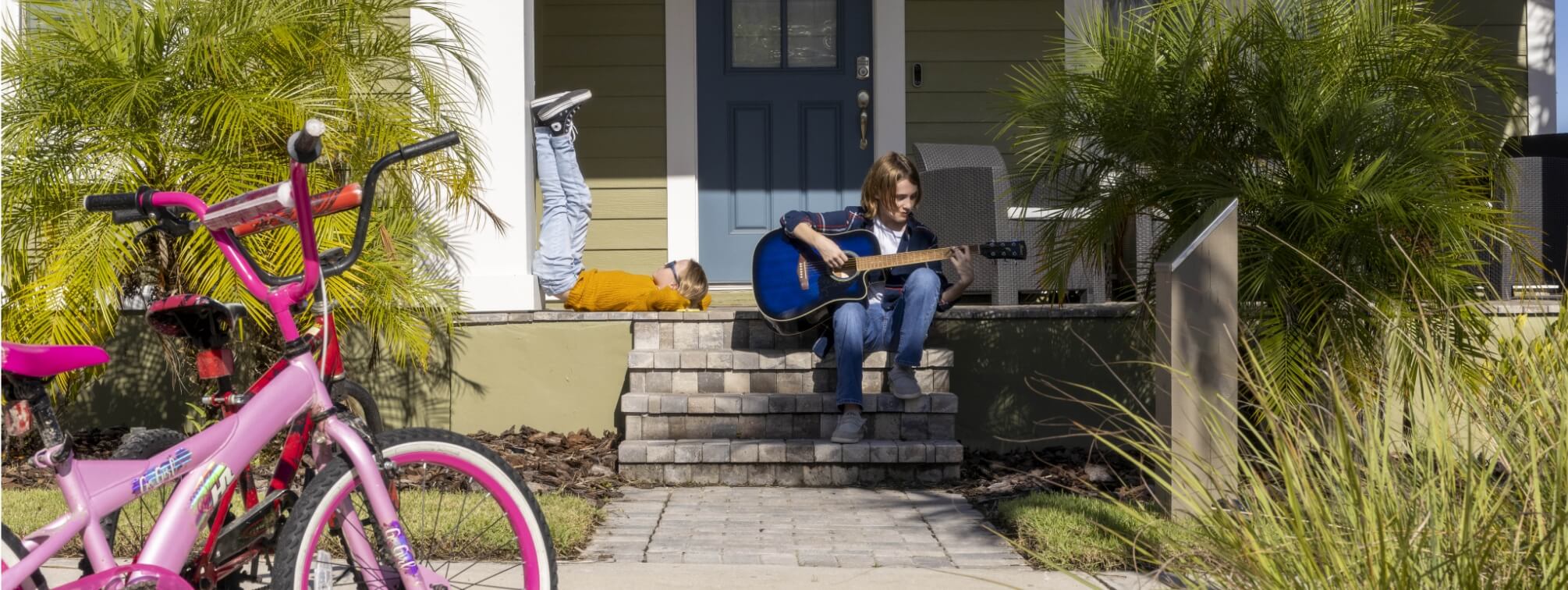 A boy sitting on a porch in Wildlight, playing guitar for his sister.